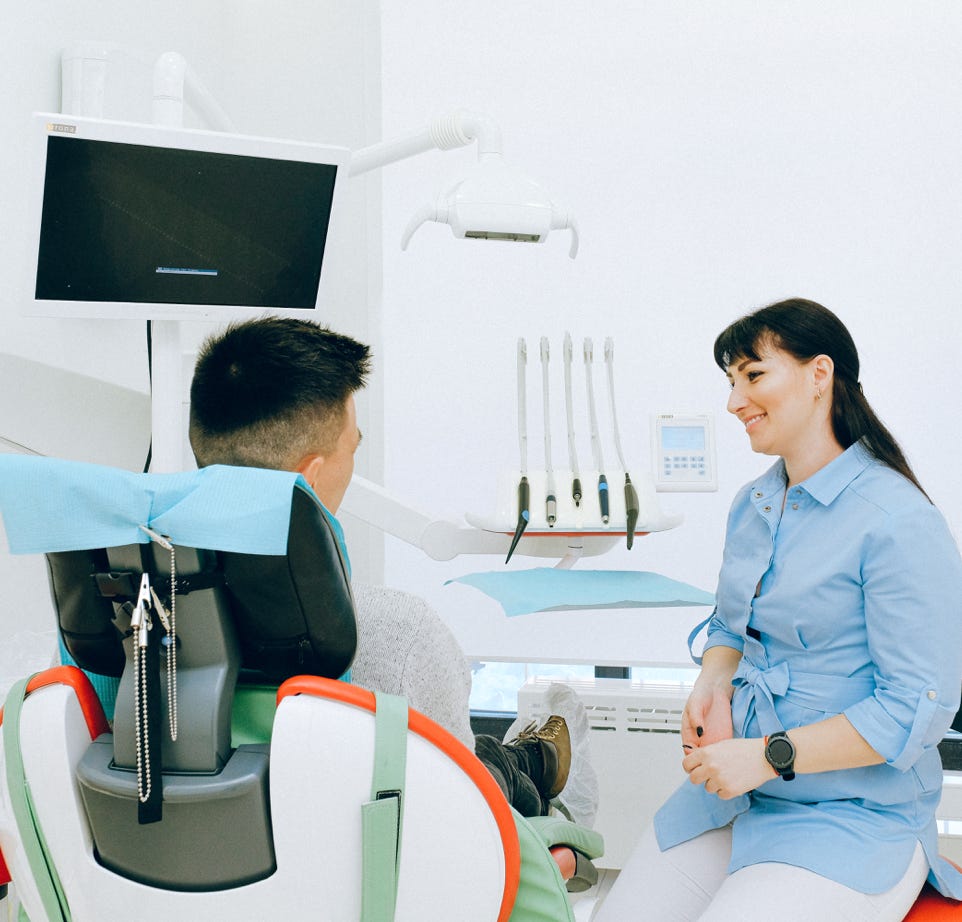 Estomatólogo Alegre Hablando Con El Paciente Sentado En El Sillón Dental